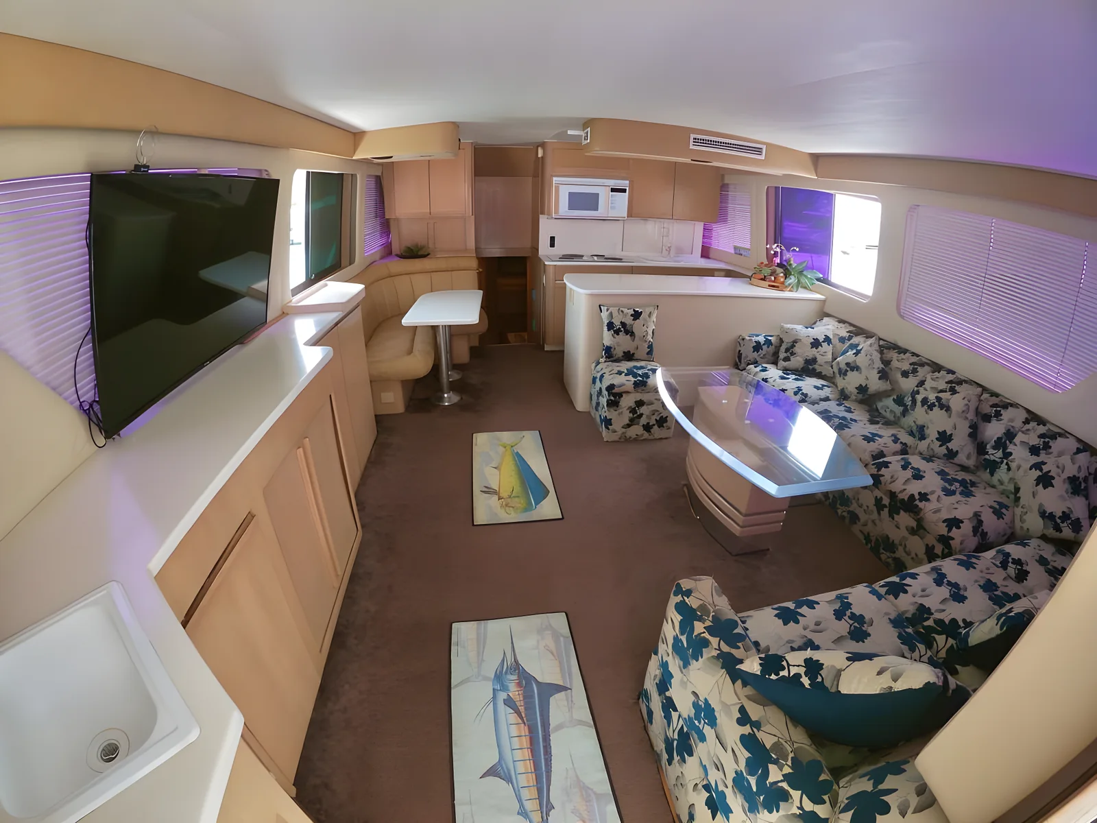 Salón interior del yate Addie con sofás, televisión y acceso a la cocina.