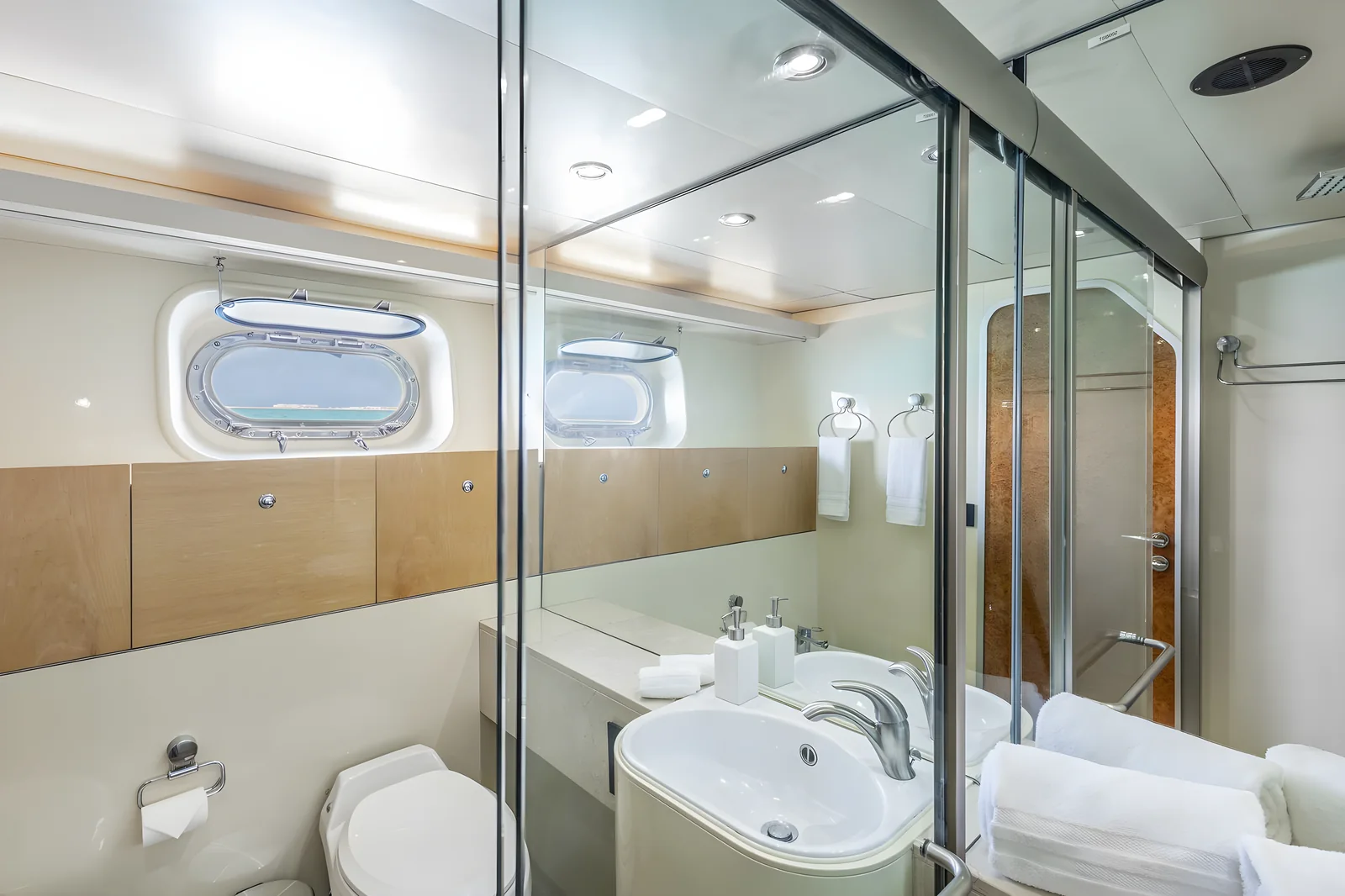 Baño elegante del yate Avalon de 115 pies con ducha de vidrio, doble lavabo y ventana de portal.