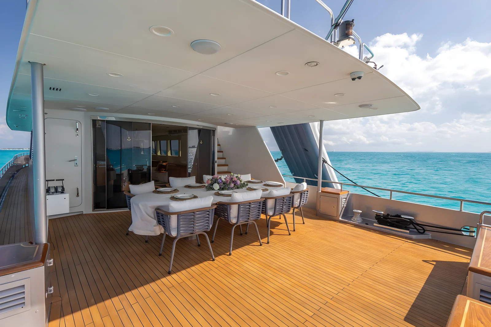 Comedor interior del yate Avalon 115ft con mesa redonda de cristal, sillas blancas y paneles de madera.