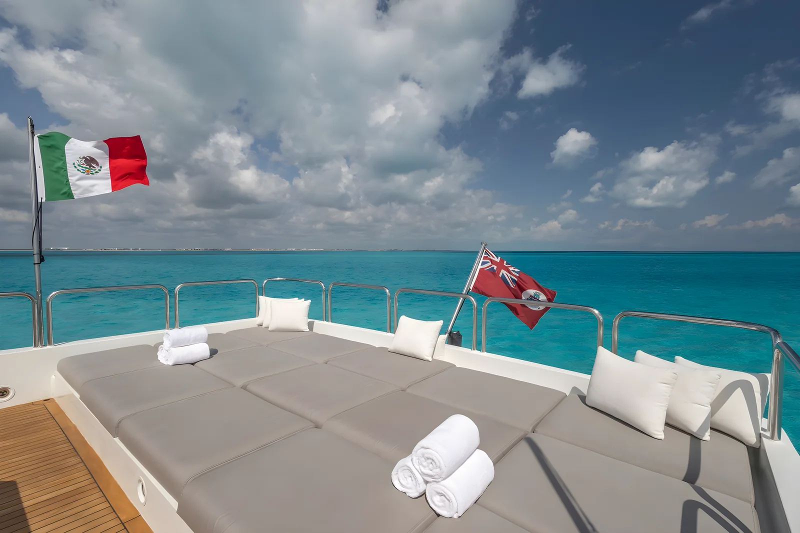 Flybridge del yate Avalon de 115 pies con amplios camastros, almohadas y banderas frente al mar.