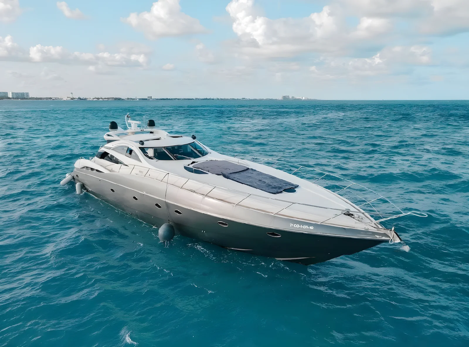 Vista aérea angular del yate Gambler de 75 pies anclado en agua turquesa con la costa al fondo.