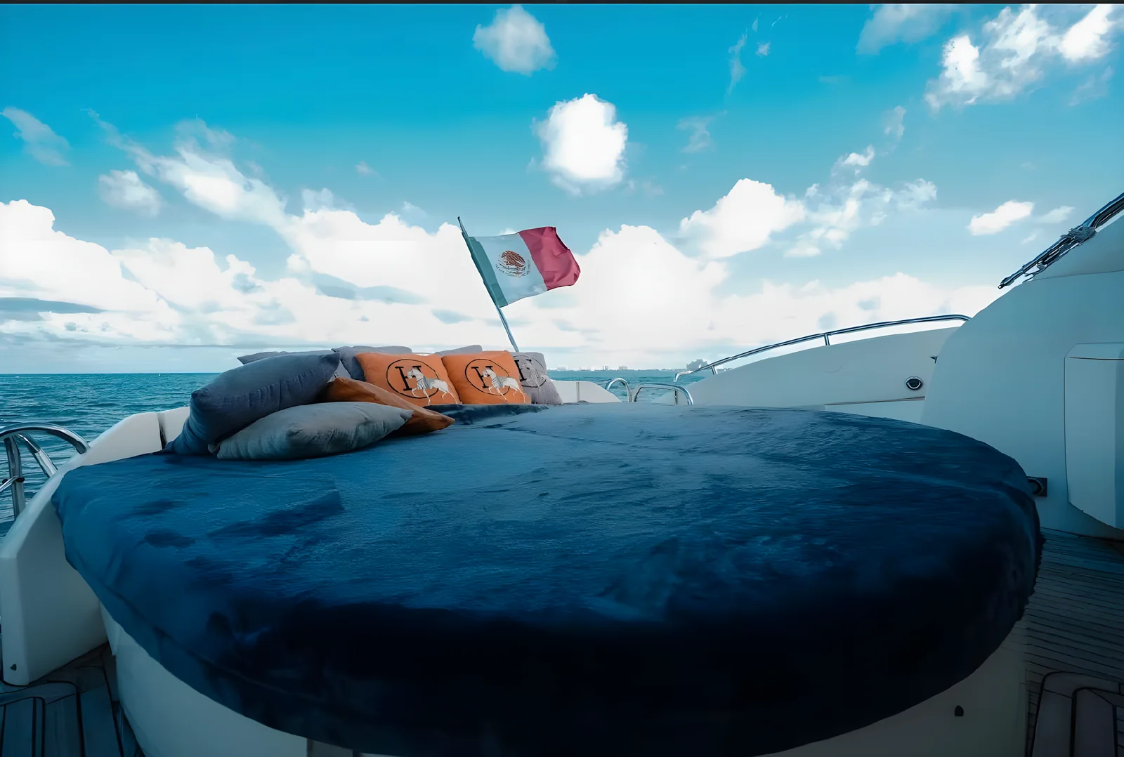 Cama solar en cubierta de proa del yate Gambler de 75 pies con cojines y bandera mexicana al fondo.