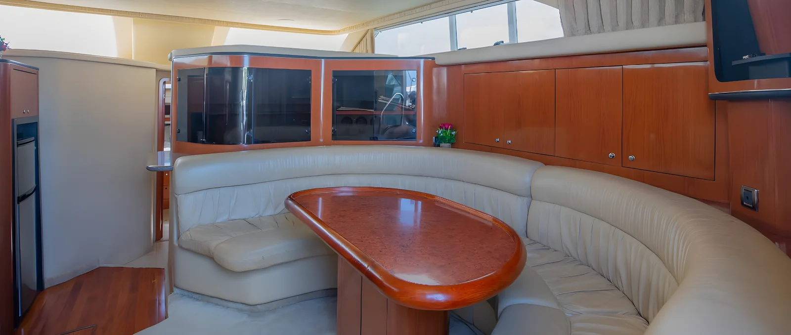 Comedor interior del yate Hercules 46ft Fly con sofá curvo y mesa ovalada de madera.
