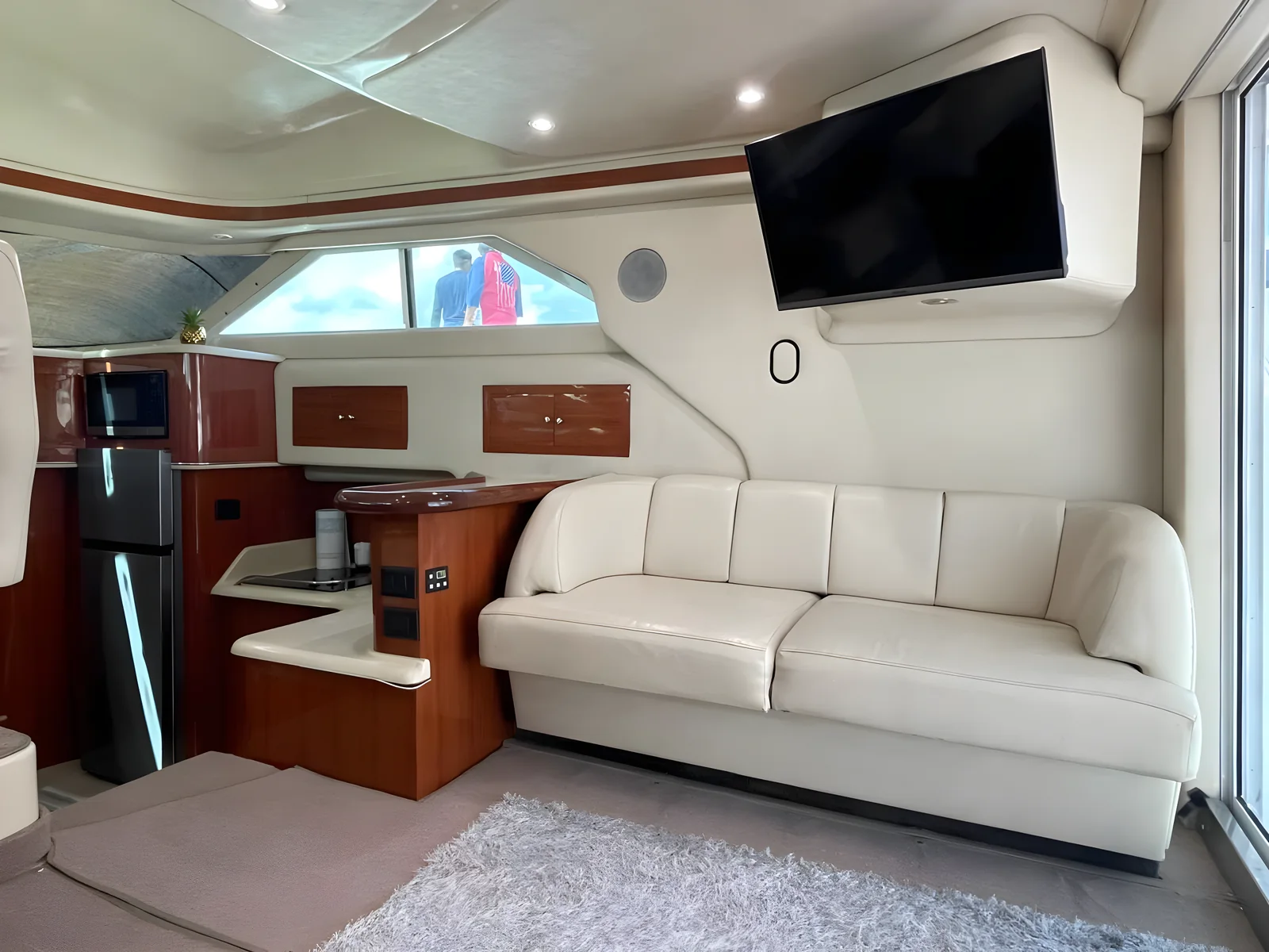 Salón del yate University Drop Out con sofá crema, barra y TV junto a ventana lateral.